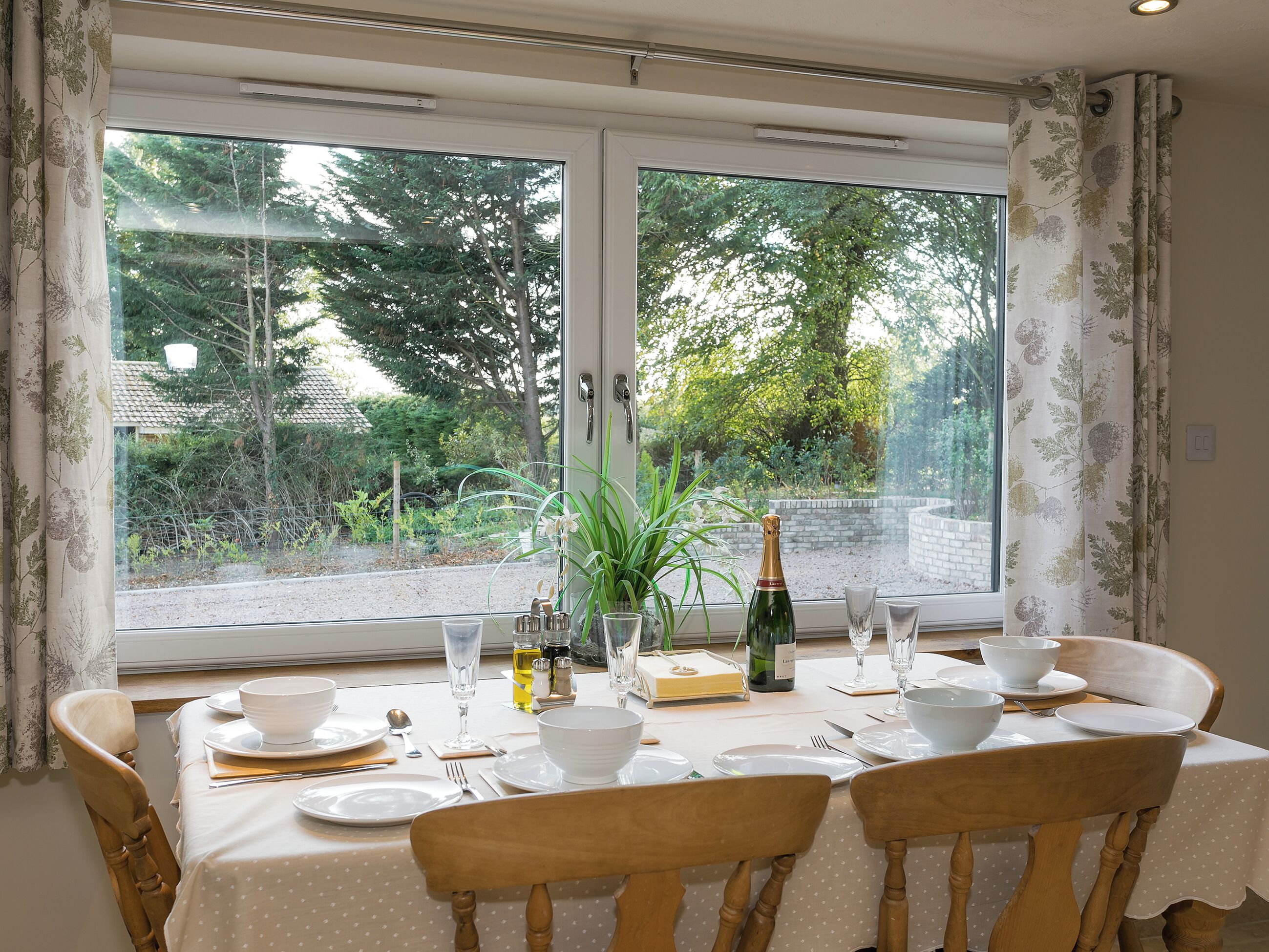 A dining table set for four with white plates, glasses, and a bottle of champagne.