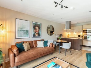 A modern living room with a brown leather sofa, a coffee table, and a dining area with a round table and chairs.