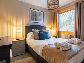 A neatly arranged bedroom with a bed, bedside lamps, a nightstand, a radiator, and a window with curtains.