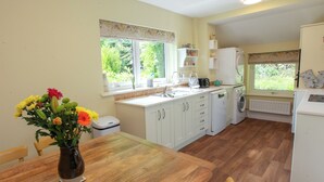 A kitchen with white cabinets, a wooden dining table, and a vase of flowers.