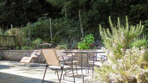 An outdoor patio with a table and chairs, surrounded by a stone wall and lush greenery.