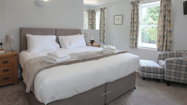 A neatly made bed with white linens, a bedside table with a lamp, and a window with curtains.