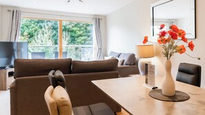 A modern living room with a sofa, a dining table, a TV, and a vase with flowers. - North Bay Sands Apartment 2- UK2630 (Scarborough)