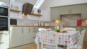 A kitchen with a dining table set for two, a microwave, oven, and a red cutting board.