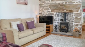 A cozy living room with a stone fireplace, a beige sofa, and a flat-screen TV.