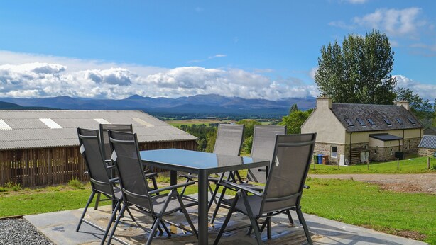 A patio with a table and chairs, a stone pathway, and a view of mountains and a house.