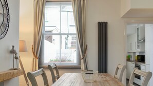 A dining area with a wooden table and chairs, a window with curtains, a radiator, and a kitchen visible through an open door. - 2 bedroom accommodation in Scarborough (Scarborough)