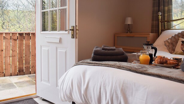 Une chambre à coucher avec un lit, une table de chevet avec une lampe, une fenêtre avec des rideaux et une vue sur l’extérieur.