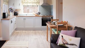 Une cuisine compacte avec des meubles blancs, une table à manger et un canapé agrémenté d’un coussin.