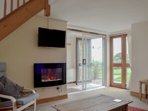 A living room with a flat-screen TV, a fireplace, a sofa, and a sliding glass door leading to a balcony. - The Stables - UKC3749 (Charmouth, near Lyme Regis)