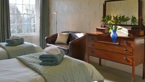 A hotel room with two beds, a wooden dresser, a chair, and a large window with curtains. - 2 bedroom accommodation in Lostwithiel (Lostwithiel)