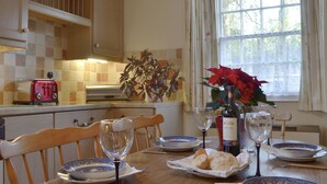 A dining table set with plates, glasses, and a bottle of wine, with a window and curtains in the background. - 2 bedroom accommodation in Lostwithiel (Lostwithiel)
