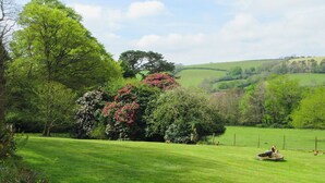 A lush green field with a variety of trees and shrubs, including some with pink flowers. - 2 bedroom accommodation in Lostwithiel (Lostwithiel)