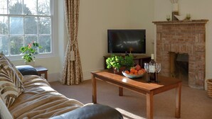 A living room with a sofa, a TV, a fireplace, and a window with curtains. - 2 bedroom accommodation in Lostwithiel (Lostwithiel)