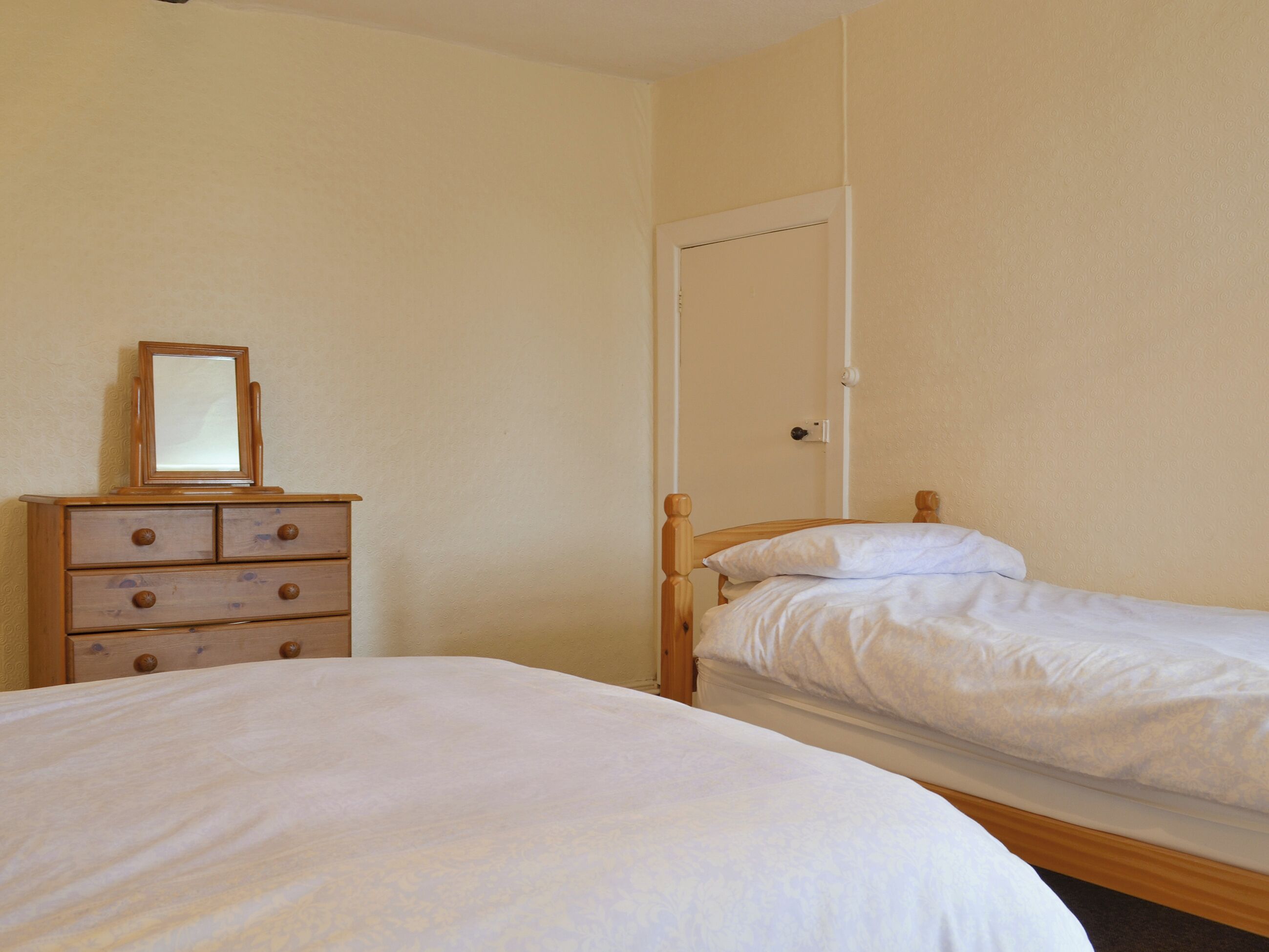 Une chambre avec un lit simple, une commode à tiroirs et une porte.