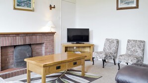 A living room with a fireplace, a television, two floral armchairs, and a sofa. - Moor Farm Cottage - UKC3734 (Foxley, near Fakenham)