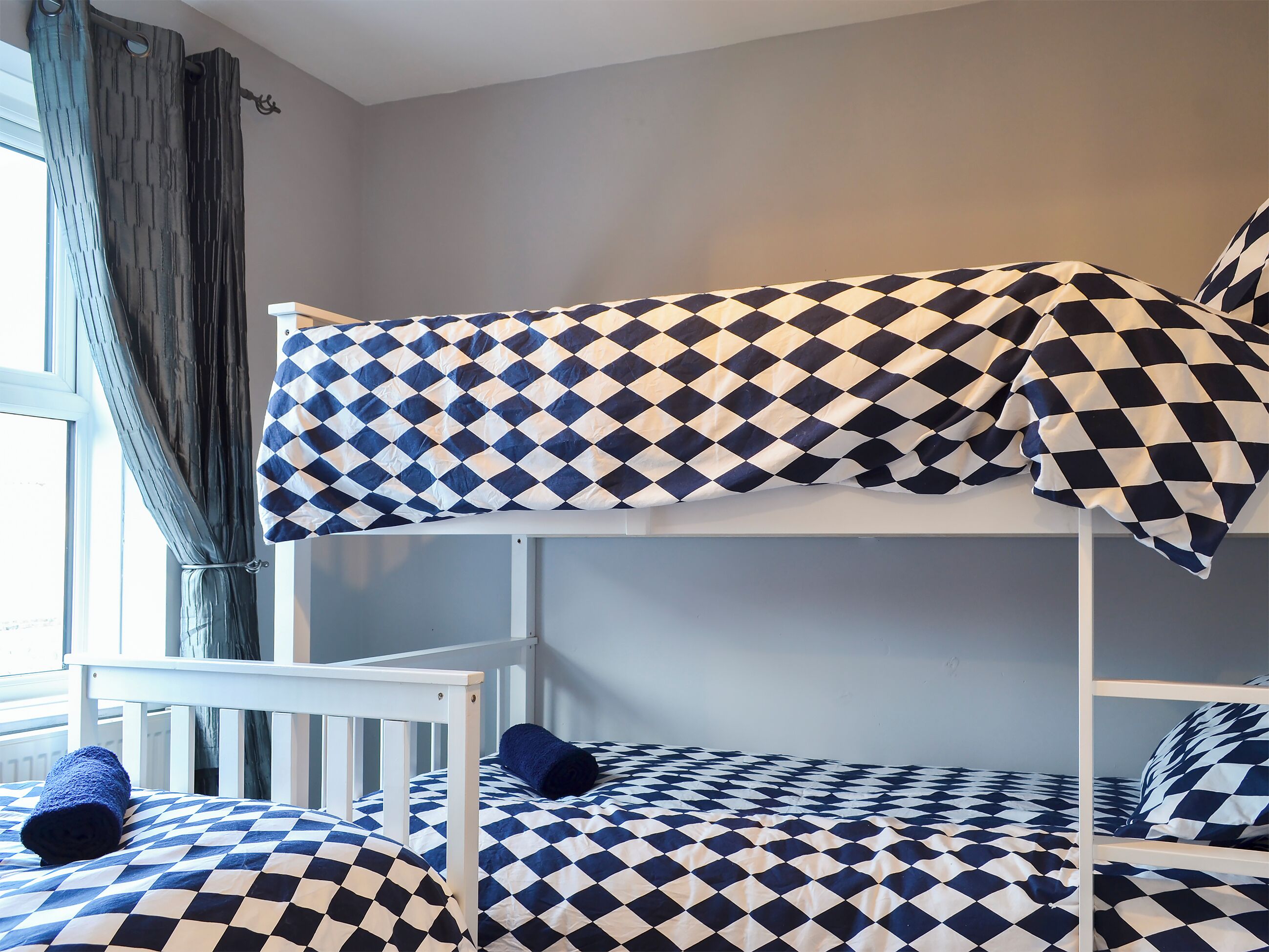 A bunk bed with a checkered bedspread and a window with curtains.