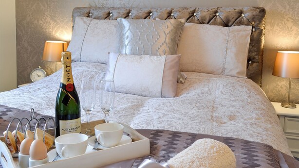 Una cama bien hecha con una botella de champán, copas y alimentos para el desayuno.