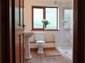 A bathroom with a toilet, a sink, a window with frosted glass, and a shower area.