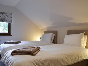 Une chambre avec deux lits, chacun doté de draps blancs et d’une tête de lit. Il y a une fenêtre donnant sur des arbres et un radiateur au mur.