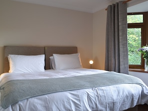 A neatly made bed with a headboard, a bedside lamp, and a window with curtains.