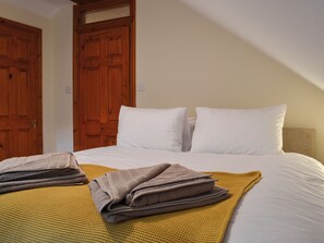 Un lit bien fait, avec des oreillers blancs et gris, une couverture jaune et des serviettes pliées sur un tapis jaune texturé.