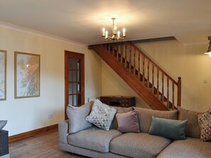 Un salon avec un escalier en bois, un canapé gris agrémenté de coussins à motifs et un lustre.