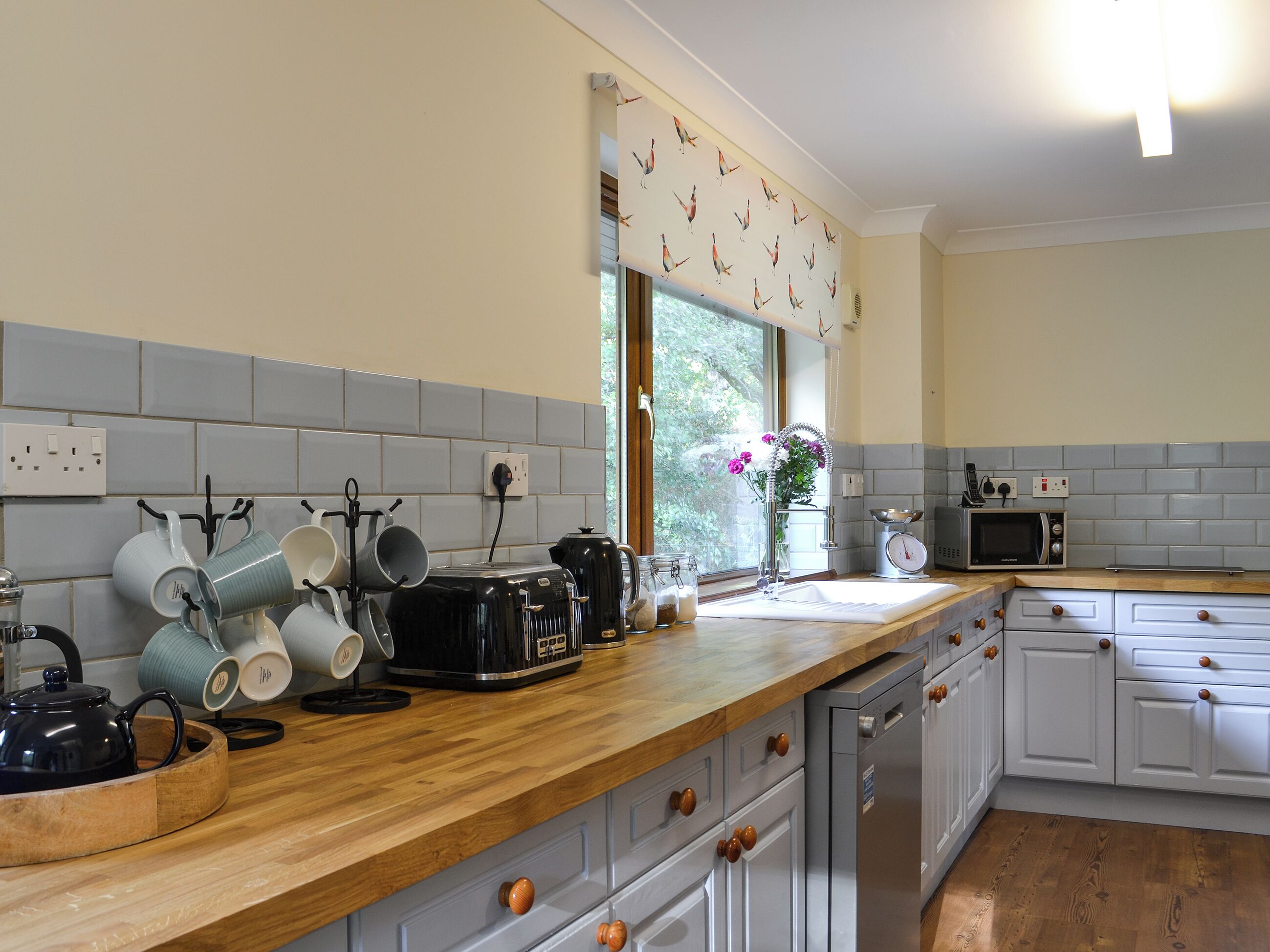 A kitchen with a wooden countertop, white cabinets, and a window with a view of trees.