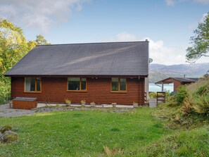 Une cabane en bois avec un toit en pente, une petite véranda et une vue sur un lac et des montagnes en arrière-plan.
