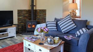 Una sala de estar acogedora con chimenea, un sofá con cojines estampados, un televisor de pantalla plana y una mesa de centro con revistas y un jarrón de flores.