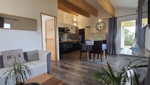 A modern living room with a sofa, coffee table, and potted plants. A dining area with a table and chairs is visible in the background. - Rental cottage in Bédoin at the foot of Mont Ventoux (Bédoin)