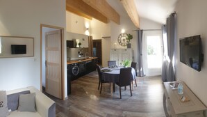 A modern kitchen with wooden beams, a dining area with a table and chairs, and a TV mounted on the wall. - Rental cottage in Bédoin at the foot of Mont Ventoux (Bédoin)