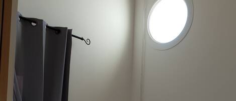 A bedroom with a bed, a small stool, a round window, and a radiator.
