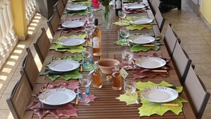 A long dining table set outdoors with chairs, plates, glasses, and a vase with flowers.