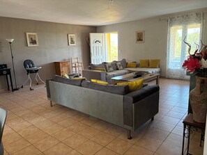 A living room with a sofa, a chair, a table, and a door leading to a balcony.
