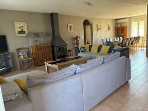 A living room with a sofa, a TV, a fireplace, a dining area with chairs, and a kitchen area with cabinets.