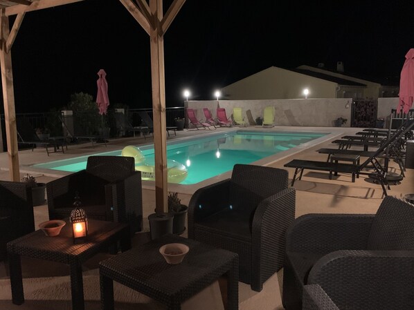 A nighttime outdoor pool area with lounge chairs and tables, a pool with floating rings, and a pergola structure. - Spacious villa with pool, near SOLENZARA, sleeps 14/16 (Solaro)