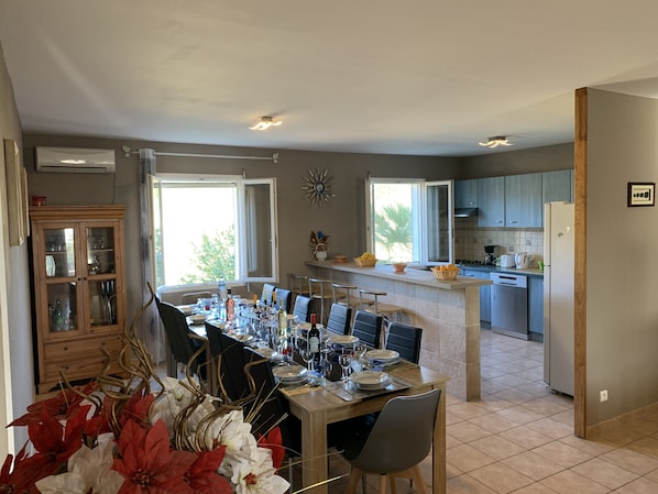 A modern kitchen with a central island, a dining area with a table set for six, and a view of the outdoors through large windows.
