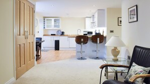 A compact living space with a kitchen, two bar stools, a dining table, and a black leather chair with a floral pillow. - 2 bedroom accommodation in Sleights, near Whitby (Sleights, near Whitby)