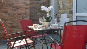 An outdoor patio with a table set for two, red chairs, and a vase with white flowers. - 2 bedroom accommodation in Sleights, near Whitby (Sleights, near Whitby)