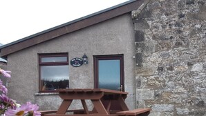 A rustic building with a stone facade, a wooden picnic table, and a sign reading "Old Stable Cottage". - 3 bedroom accommodation in Uplawmoor, near Barrhead (Uplawmoor, near Barrhead)