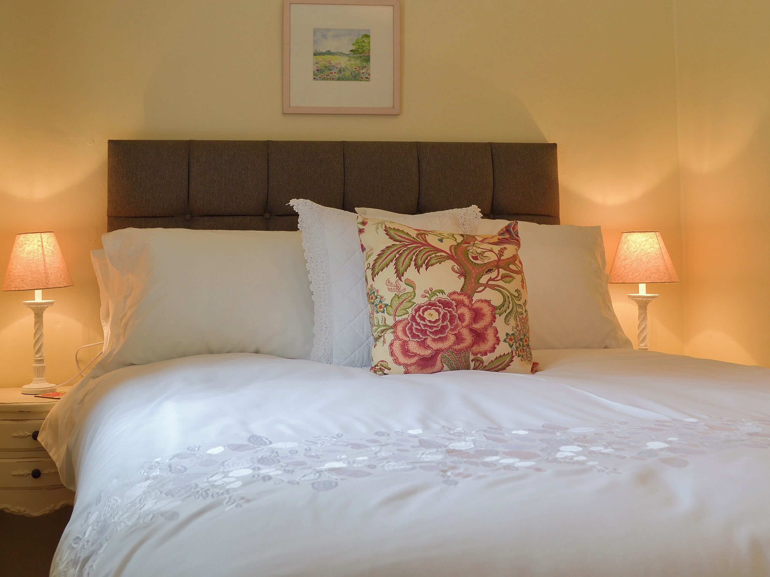 A neatly made bed with white linens and decorative pillows, flanked by two bedside lamps.