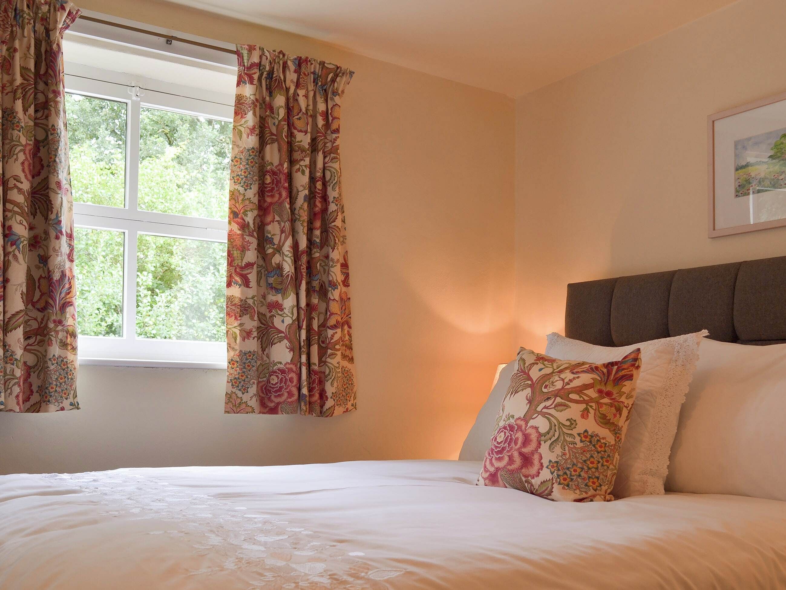 Een slaapkamer met een bed, bloemen gordijnen, en een lijst met een afbeelding aan de muur.