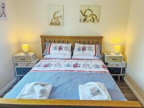A neatly made bed with a checkered bedspread and two pillows with a lighthouse design, flanked by bedside tables with lamps and a wall-mounted artwork above. - Flat 1 Portman House (Shanklin)