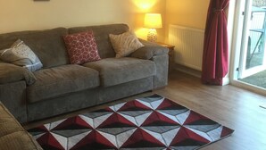 Un salon avec un canapé, des coussins à motifs, un tapis à motifs géométriques, une lampe et une fenêtre avec des rideaux.