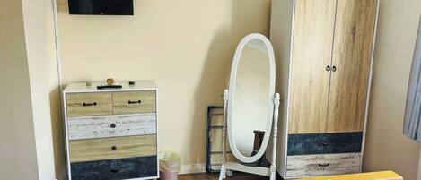 A bedroom with a bed, a dresser, a wardrobe, a mirror, and a television.