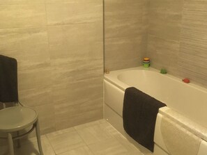 Et badeværelse med badekar, et lille rundt bord og et håndklæde hængende på væggen.