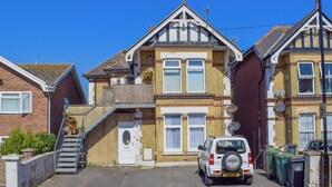 Une maison à deux étages avec un jardin devant, un escalier menant à l’entrée et une voiture garée.