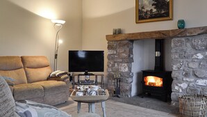 A cozy living room with a stone fireplace, a flat-screen TV, and a comfortable sofa. - 3 bedroom accommodation in Middleton, near Swansea (Middleton, near Swansea)