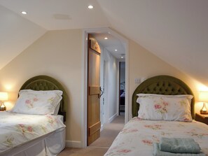 A bedroom with two beds, each with a green upholstered headboard, white floral bedding, and bedside lamps.